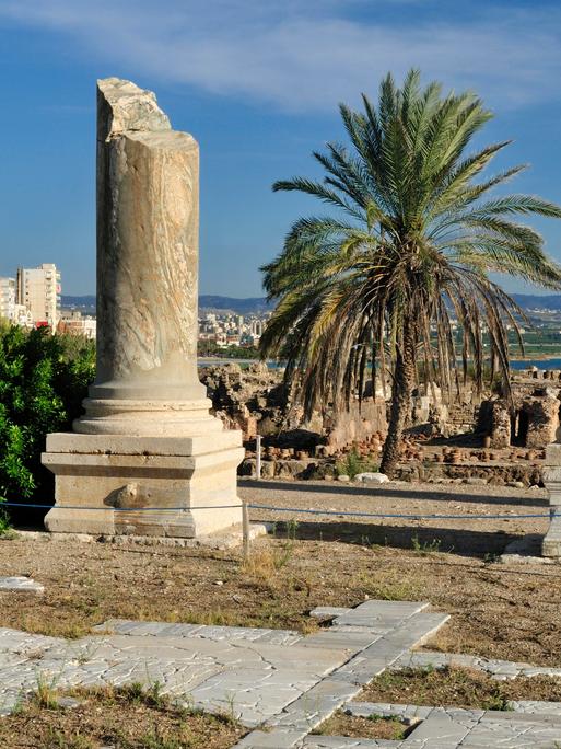 Archäologische Ausgrabungsstätte von Tyros im Libanon. Zwei große antike Säulen stehen zwischen Palmen und einer Moschee.