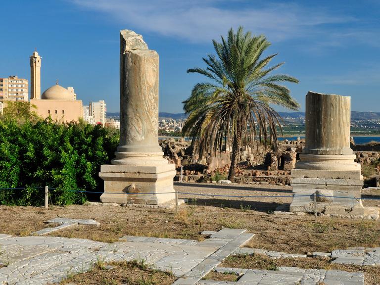 Archäologische Ausgrabungsstätte von Tyros im Libanon. Zwei große antike Säulen stehen zwischen Palmen und einer Moschee.