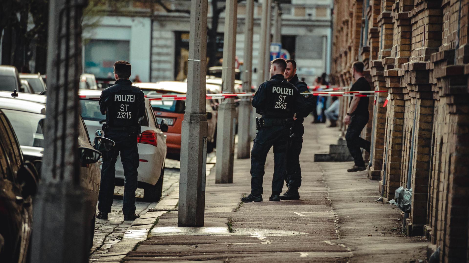 Polizei steht vor einem Wohnhaus in Halle, ein Bereich ist mit Flatterband abgesperrt.
