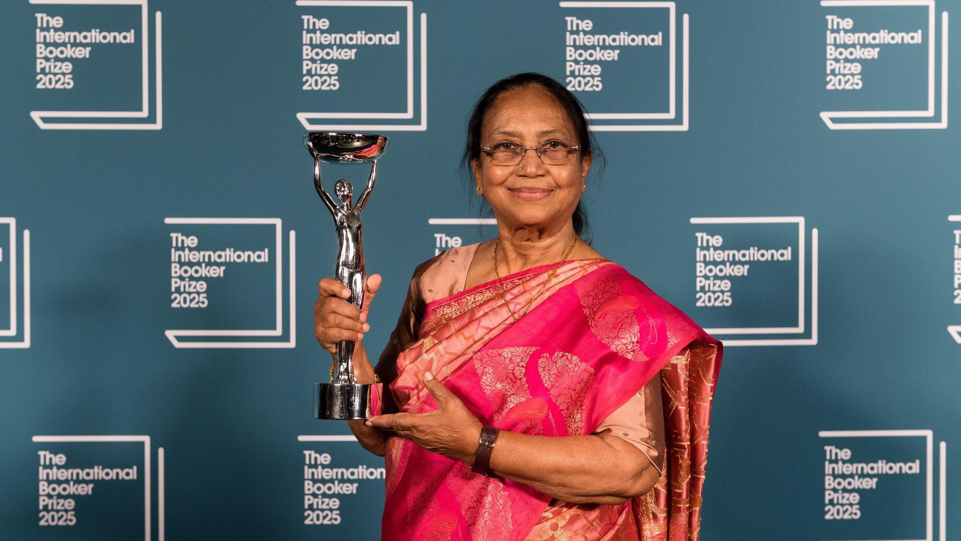 Banu Mushtaq hält eine Trophäe in den Händen, hinter ihr eine blaue Wand mit der Aufschrift "The International Booker Prize 2025" Banu Mushtaq hält eine Trophäe in den Händen, hinter ihr eine blaue Wand mit der Aufschrift "The International Booker Prize 2025"