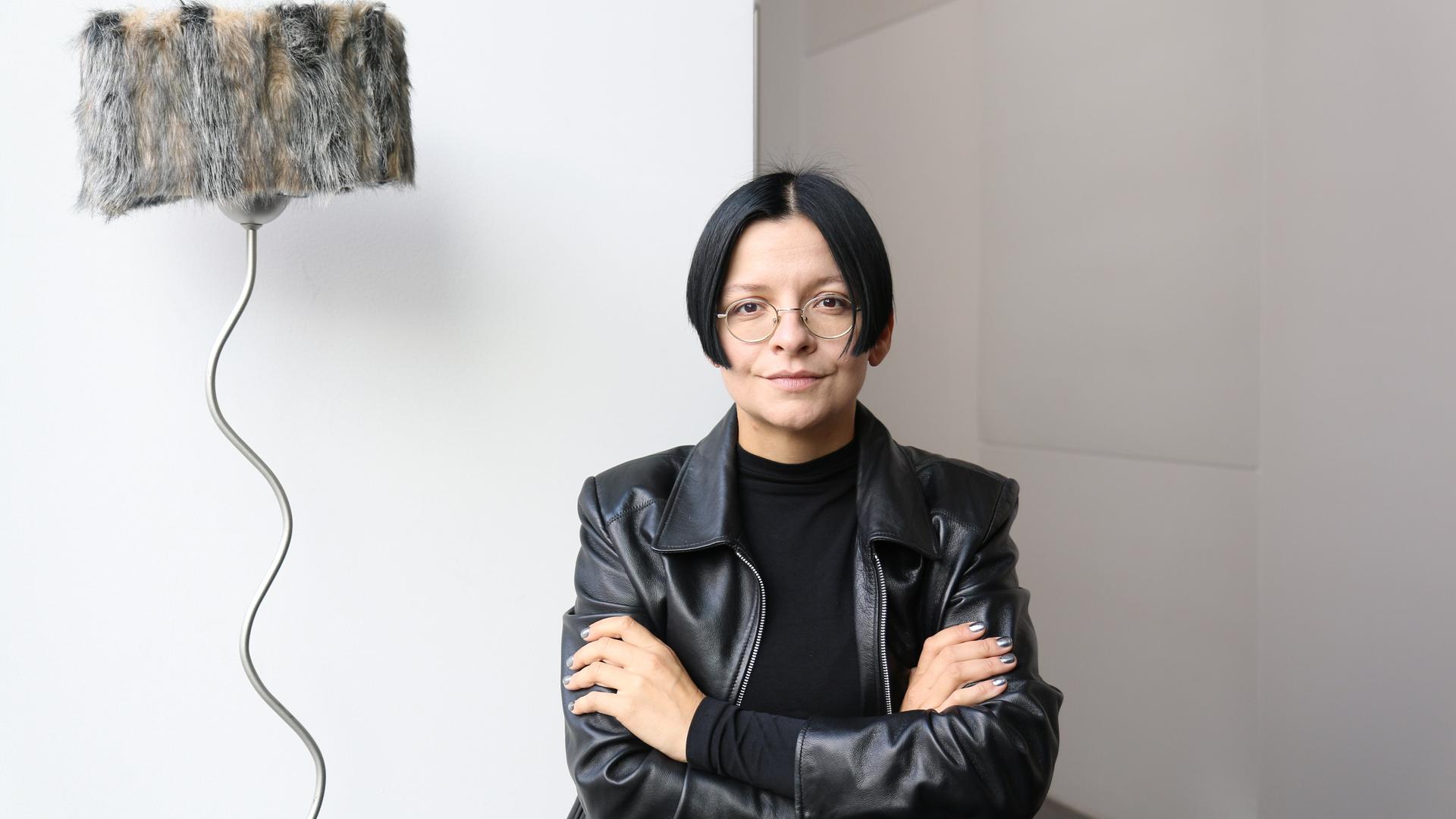 Die Installationskünstlerin Henrike Naumann in schwarzer Lederjacke vor einem ihrer Werke. 
