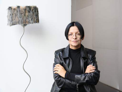 Die Installationskünstlerin Henrike Naumann in schwarzer Lederjacke vor einem ihrer Werke. 
