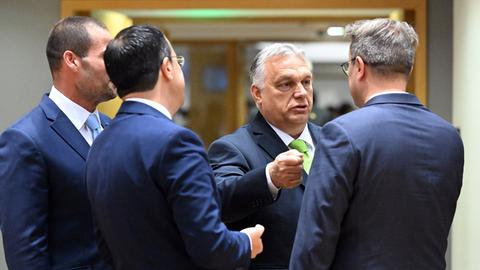 Männer in Anzügen stehen in einem Raum zusammen und unterhalten sich.