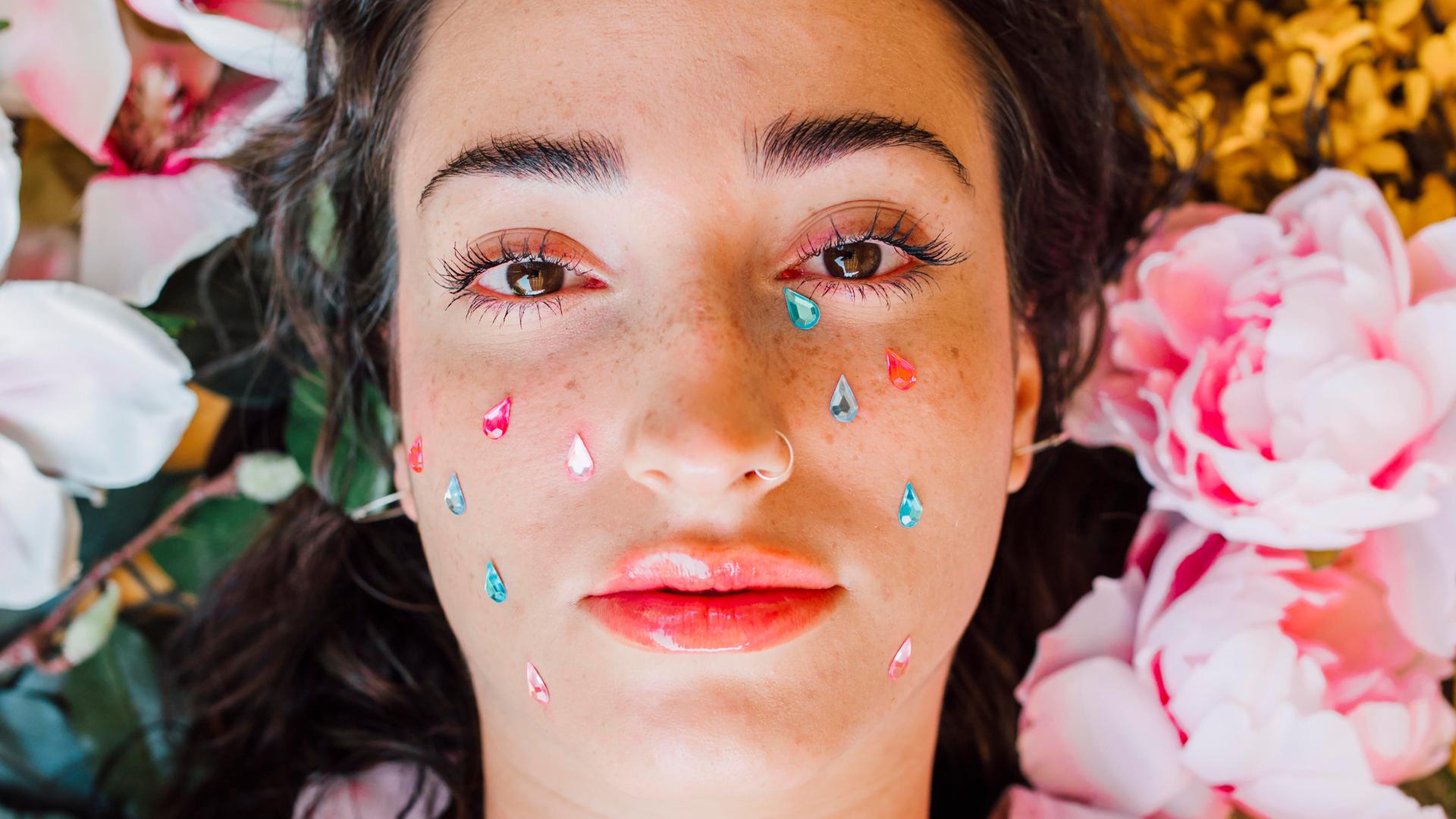 Porträt einer Frau, deren Gesicht mit Stickern in Form bunter Tränen beklebt ist.