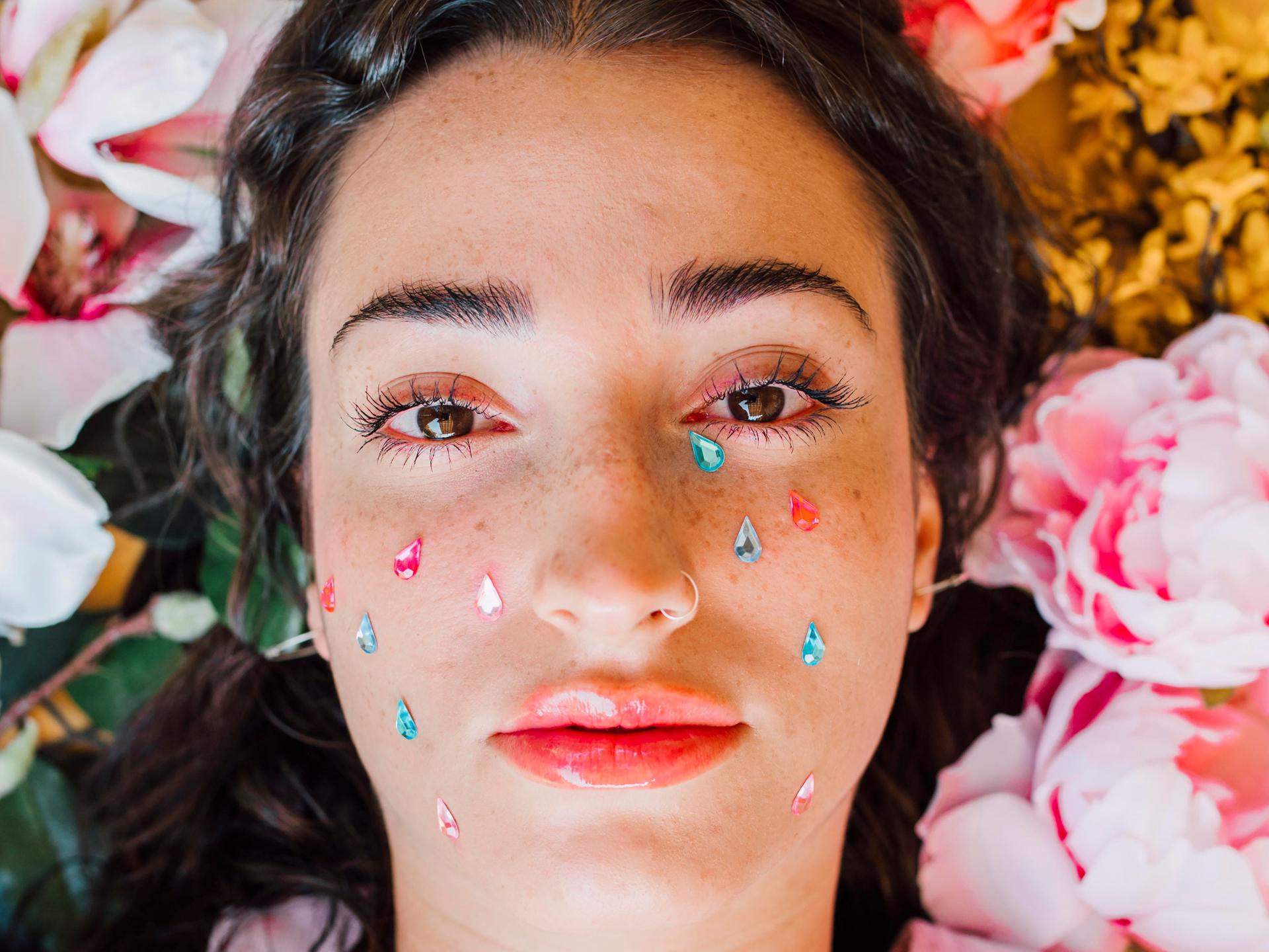 Porträt einer Frau, deren Gesicht mit Stickern in Form bunter Tränen beklebt ist.