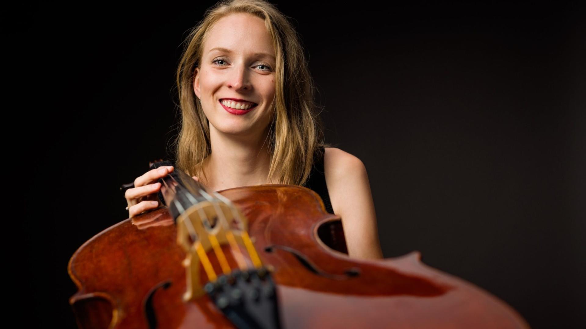 Marie-Elisaveth Hecker blickt lachend in die Kamera, während sie ihr Cello zur Kamera reckt. 