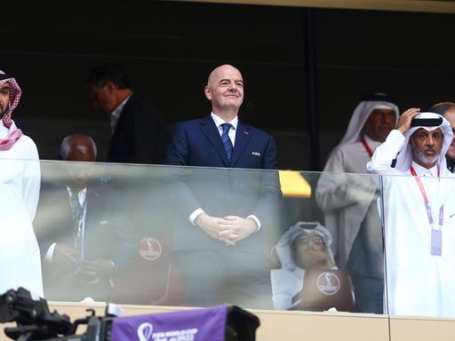 FIFA-Präsident Gianni Infantino bei dem WM in Katar auf der Tribüne. Neben ihm stehen saudische Offizielle. 