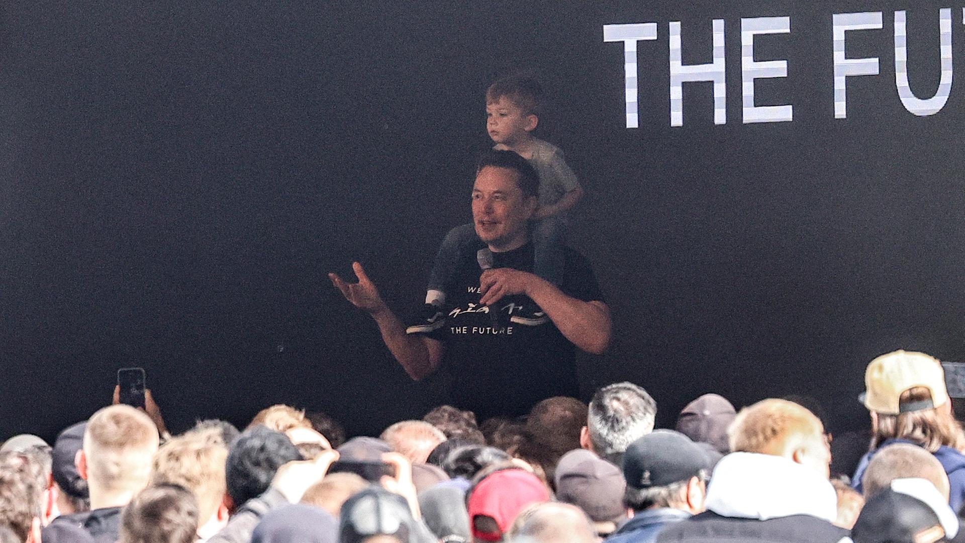Tesla-Chef Elon Musk betritt eine Bühne mit seinem Sohn auf den Schultern in der Tesla Gigafactory für Elektroautos in Grünheide bei Berlin.
