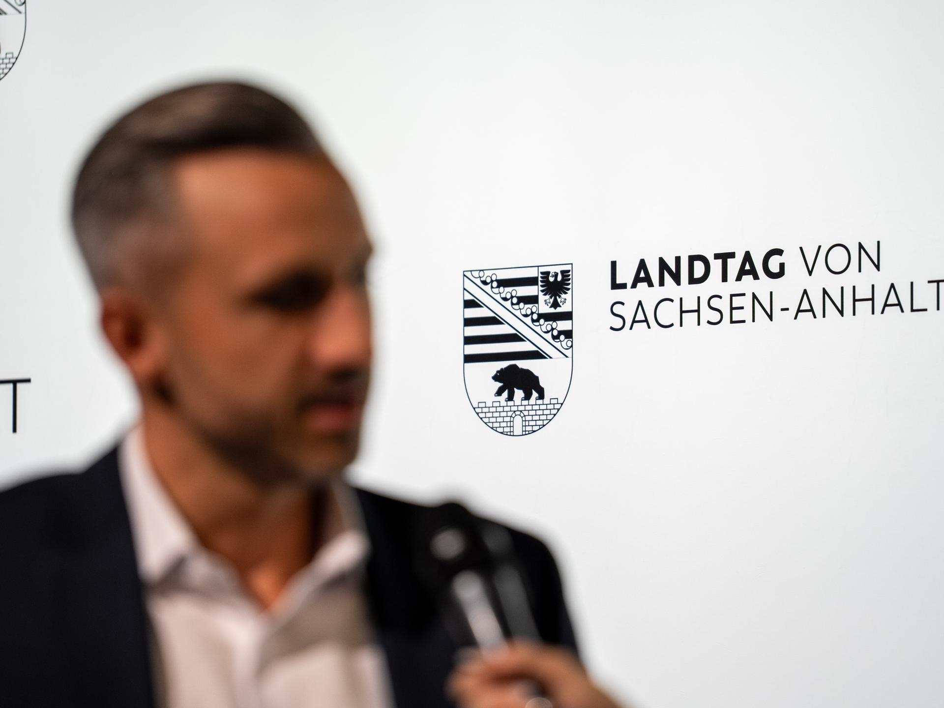 Ein Mann steht vor einer Wand mit der Aufschrift "Landtag von Sachsen-Anhalt". Er wird von einem Journalisten mit Mikrofon befragt, ist aber nur verschwommen zu erkennen. Es ist der AfD-Politiker Ulrich Siegmund. Ein Mann steht vor einer Wand mit der Aufschrift "Landtag von Sachsen-Anhalt". Er wird von einem Journalisten mit Mikrofon befragt, ist aber nur verschwommen zu erkennen. Es ist der AfD-Politiker Ulrich Siegmund.