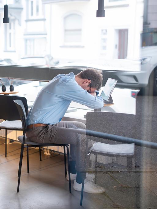 Geschäftsmann, der über seinem Tablet in einem Café ein Nickerchen macht