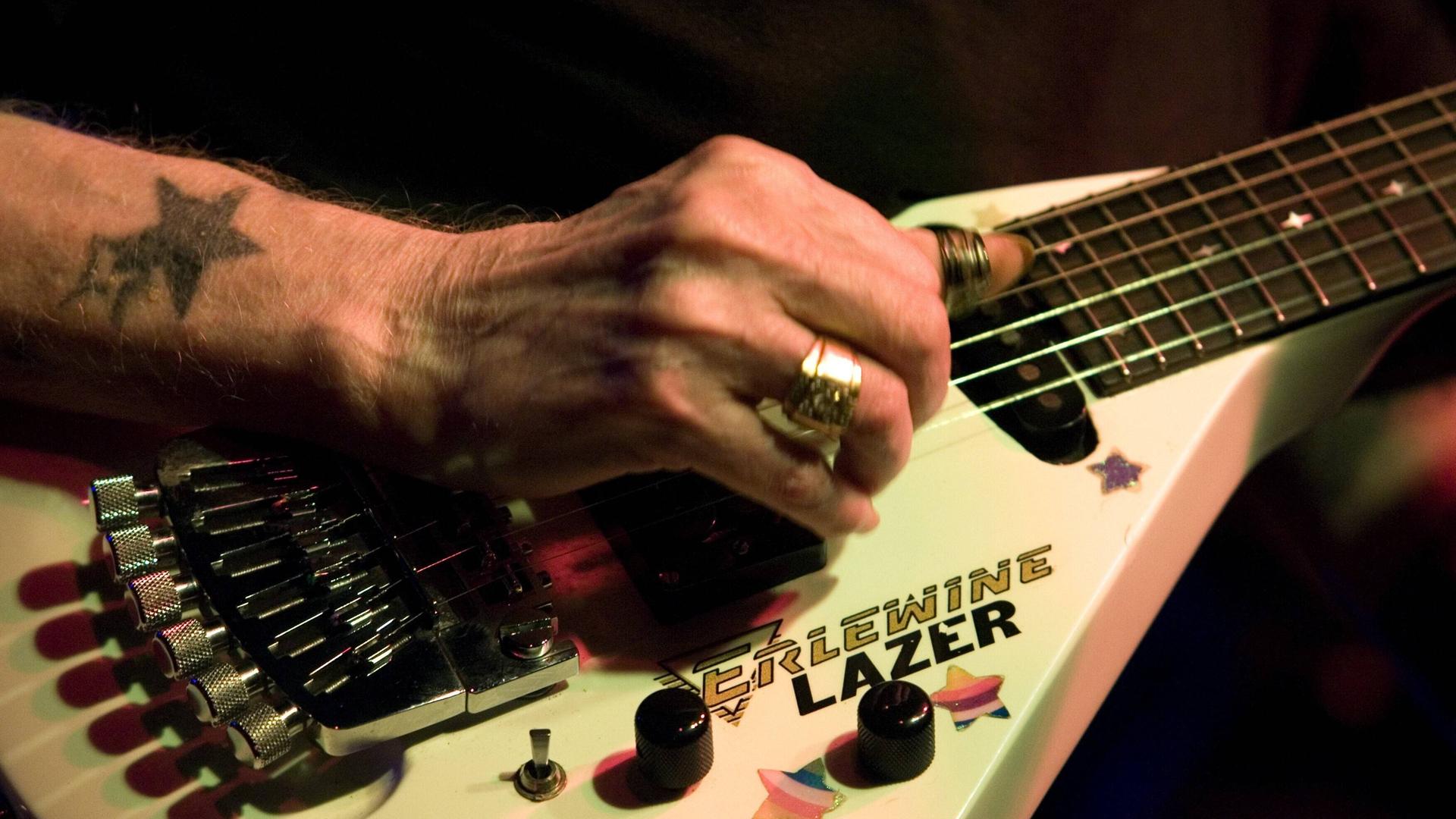 Blick auf die Hand von Gitarrist Johnny Winter, der Ringe trägt und auf seiner mit Aufklebern überhäufte E-Gitarre spielt.