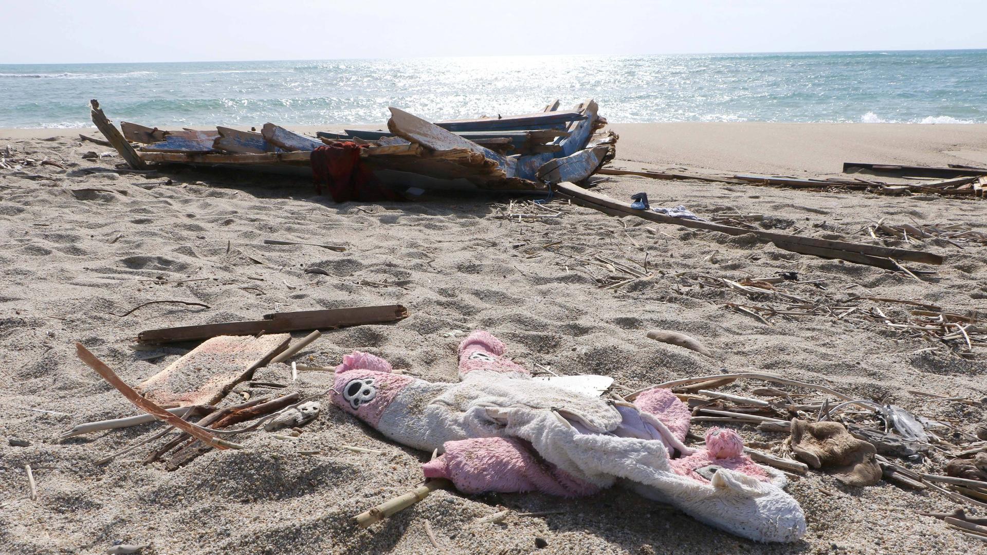 Trümmer von dem Boot und ein Kuschel-Tier liegen an einem Strand.