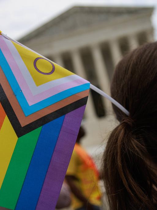 Student hält eine inklusive LBTGQ Flagge vor dem Supreme Court in der Hand