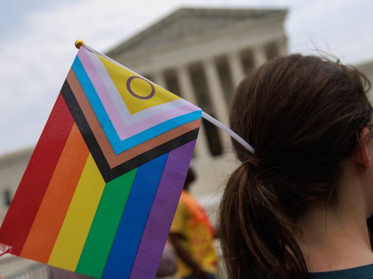 Student hält eine inklusive LBTGQ Flagge vor dem Supreme Court in der Hand