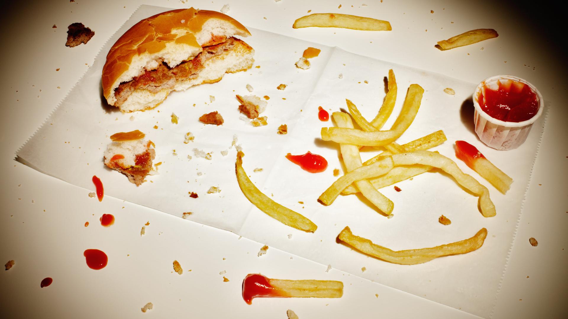 Ein angebissener Burger und Reste von Pommes liegen auf einem Tisch.