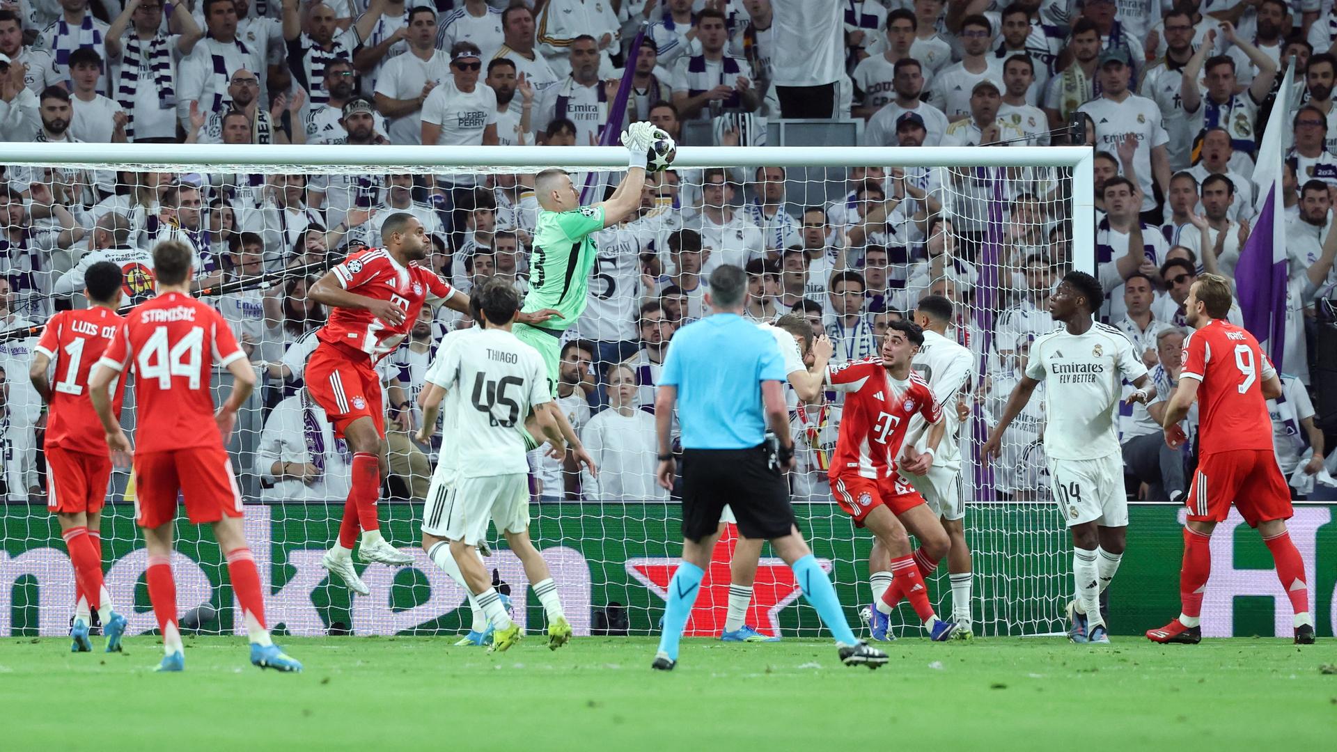 Real Madrids Torhüter Andriy Lunin springt in seinem Strafraum in die Höhe und fängt den Ball. Um ihn herum sind mehrere Spieler von Real und Bayern München. 