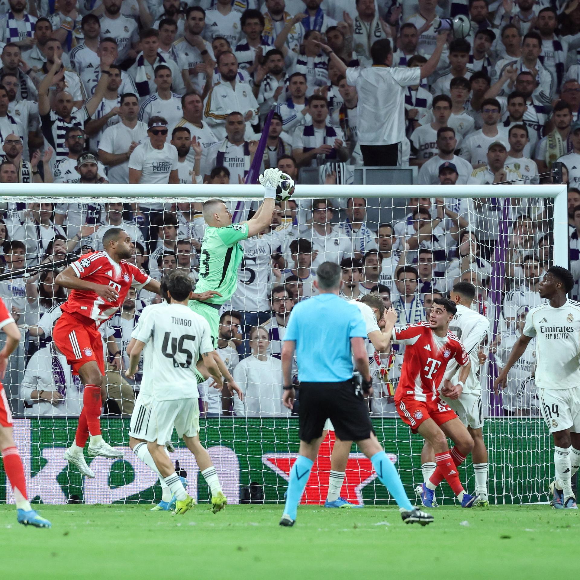 Real Madrids Torhüter Andriy Lunin springt in seinem Strafraum in die Höhe und fängt den Ball. Um ihn herum sind mehrere Spieler von Real und Bayern München. 