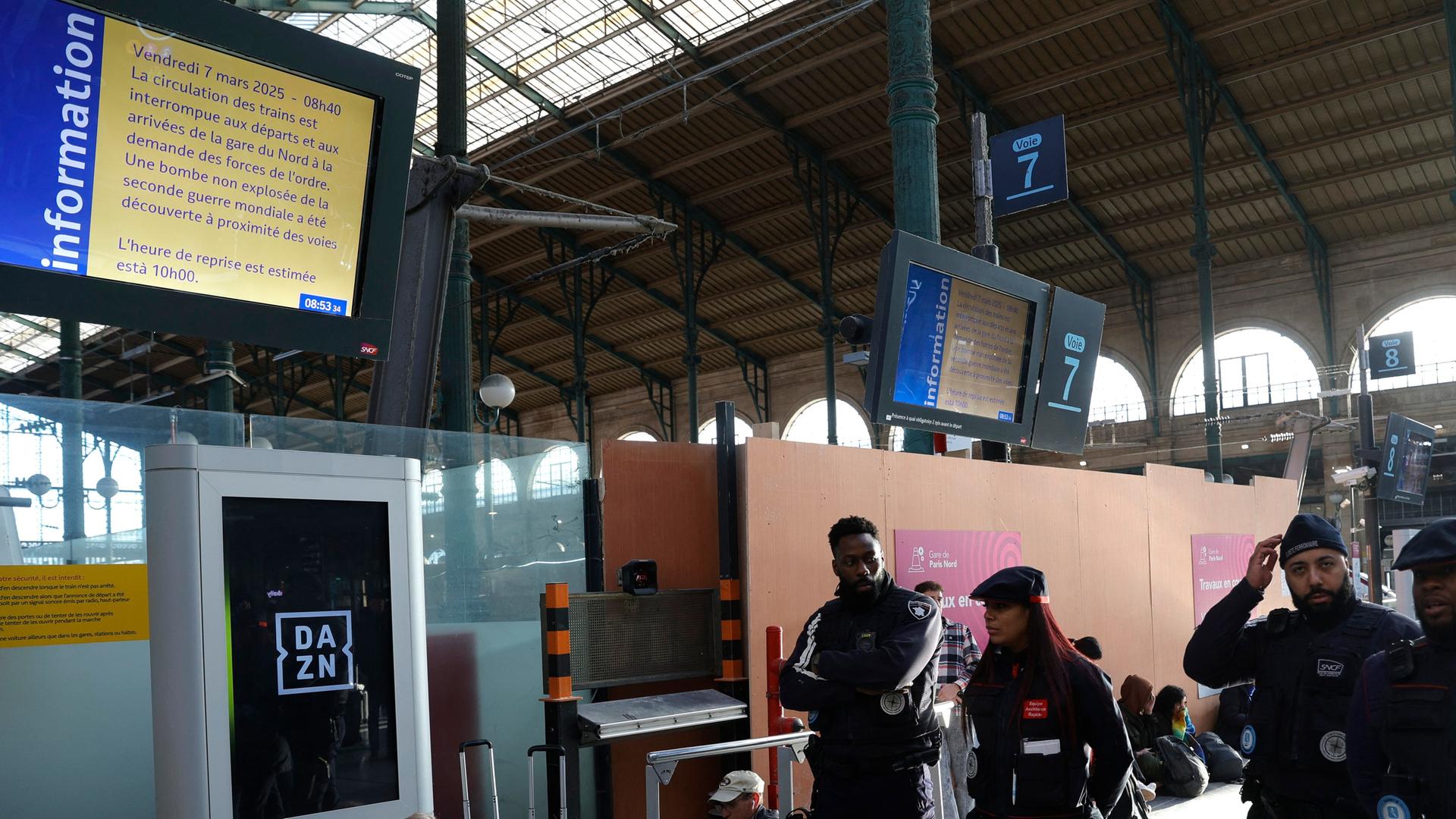 Sicherheitsleute gehen am Bahnhof Gare du Nord an einem großen Bildschirm vorbei, auf dem darüber informiert wird, dass Züge wegen des Funds einer Weltkriegsbombe ausfallen.