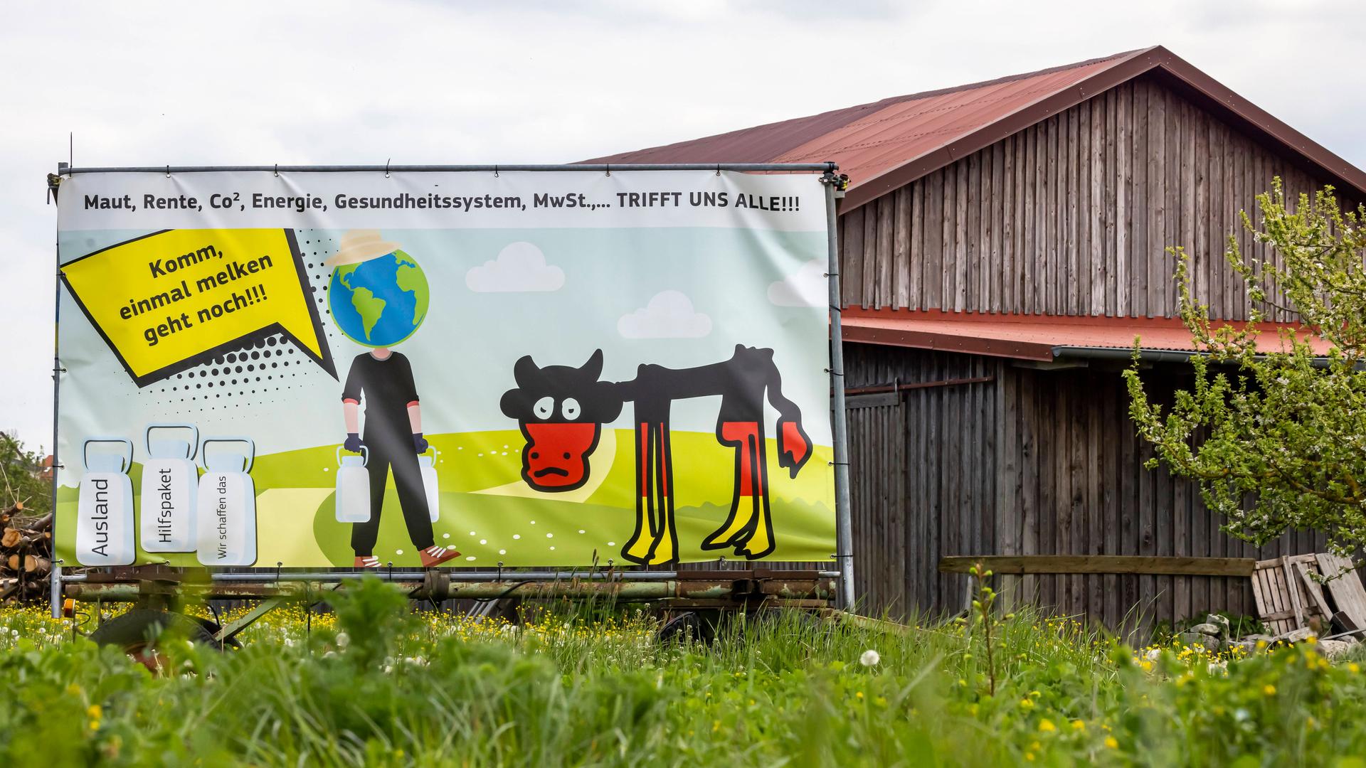 Zu sehen ist ein Plakat vor einer Scheune mit einer abgemagerten Kuh und daneben ein Mann mit Weltkugel als Kopf, der zur Kuh sagt, "Komm, einmal melken geht noch!"