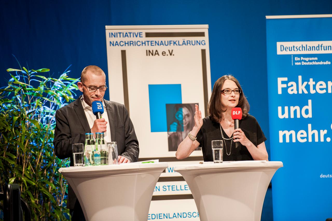 Eine Frau und ein Mann stehen auf einer Bühne und sprechen ins Mikrofon.