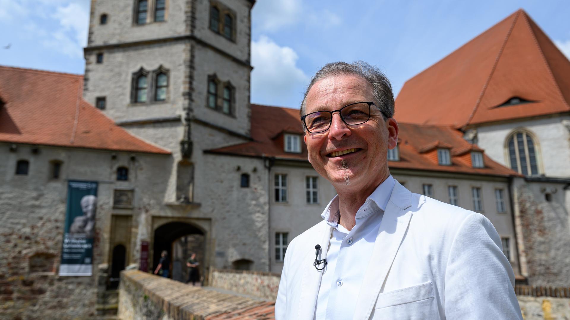 Thomas Bauer-Friedrich, Direktor des Kunstmuseums Moritzburg, steht am Tor zur Moritzburg in Halle/Saale. Er trägt einen hellen Anzug. Im Hintergrund ist die Burg zu erkennen.