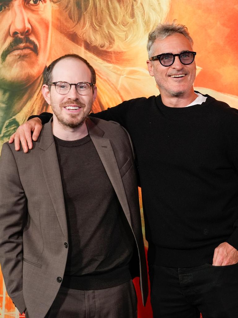 Regisseur Ari Aster (li.) und Schauspieler Joaquin Phoenix bei der Premiere ihres gemeinsamen Films Ellington. Beide lächeln vergnügt, im Hintergrund das überdimensionale Poster ihres Films. 