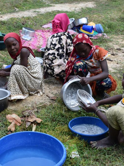 Junge Frauen in Pemba, Tansania waschen Plastikschüsseln und Töpfe auf dem Boden hockend ab.