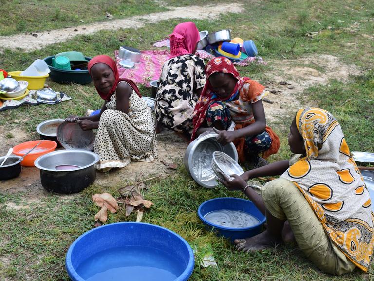 Junge Frauen in Pemba, Tansania waschen Plastikschüsseln und Töpfe auf dem Boden hockend ab.