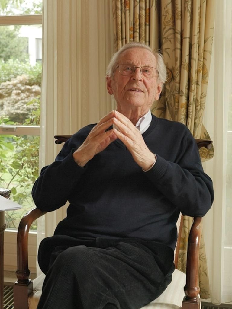 Klaus Adlung sitzt als alter Mann in einem Sessel in seinem Wohnzimmer, im Hintergrund ein Fenster mit Gardine. 