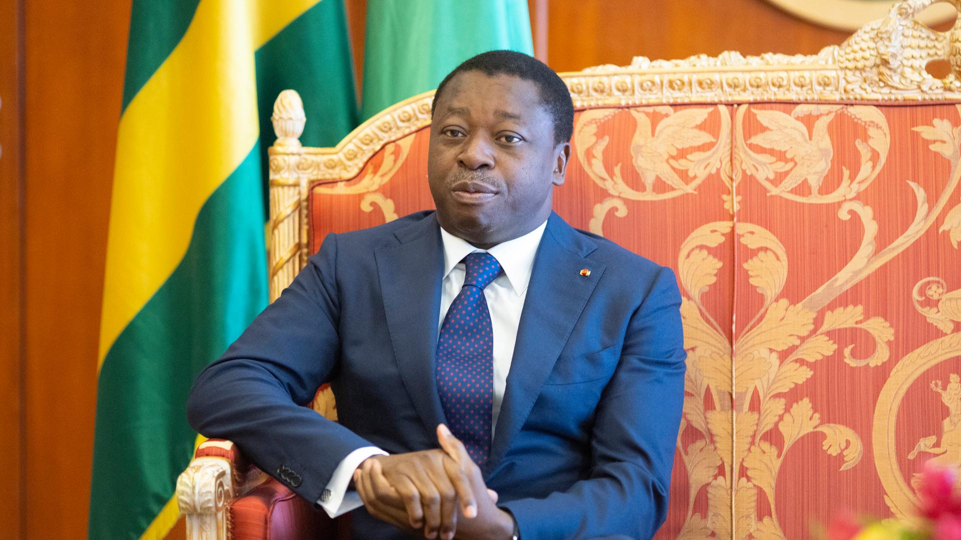 Faure Gnassingbé sitzt auf einem vergoldeten Sessel, hinter ihm die Flagge Togos. 