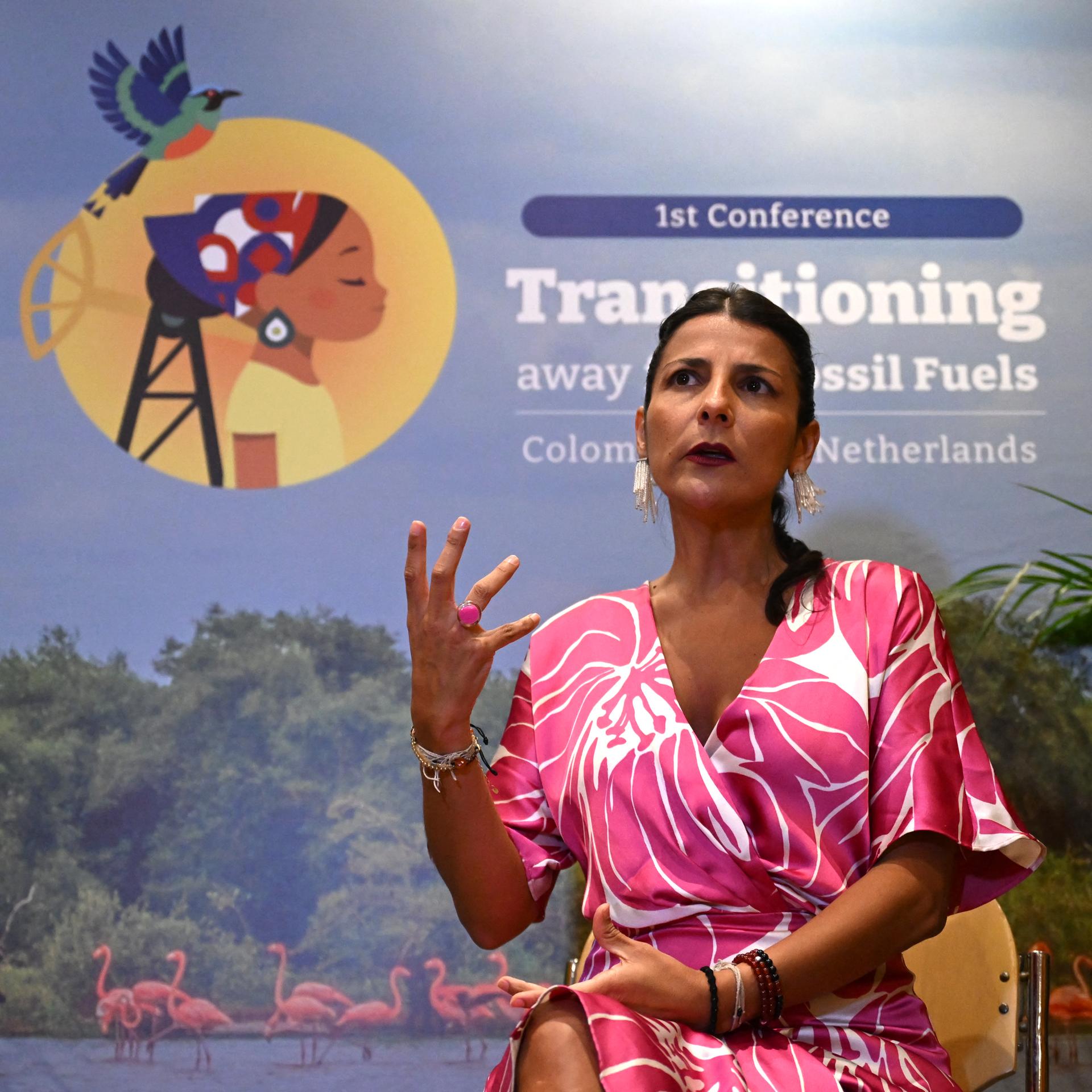 Ministerin Vélez Torres spricht auf einer Veranstaltung der Konferenz. Sie gestikuliert mit einer Hand und schaut ernst an der Kamera vorbei. Im Hintergrund ist ein Plakat mit dem Logo der Konferenz zu sehen. 