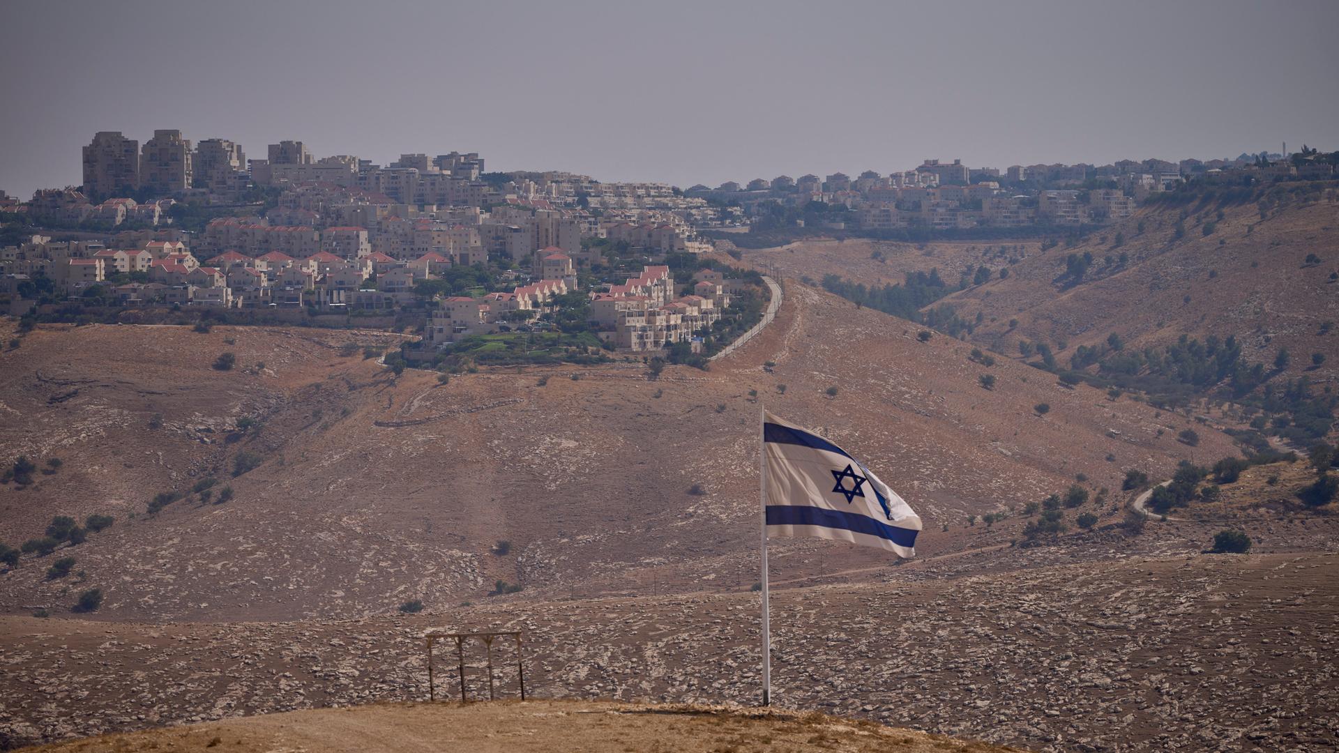 Eine israelische Flagge auf einem Hügel. Im Hintergrund ist eine Siedlung zu sehen. Eine israelische Flagge auf einem Hügel. Im Hintergrund ist eine Siedlung zu sehen.