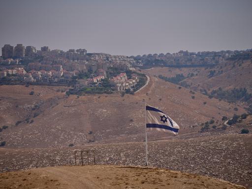 Eine israelische Flagge auf einem Hügel. Im Hintergrund ist eine Siedlung zu sehen. 