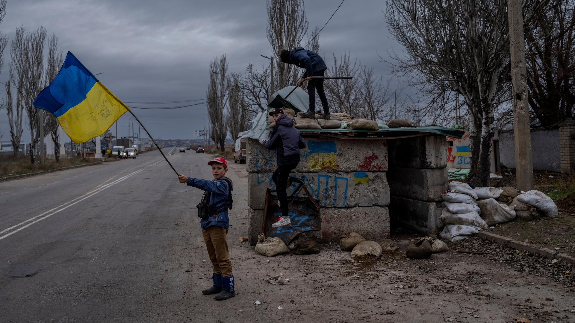 Ukrainische Kinder an einem verlassenen Kontrollpunkt bei Cherson. Eines schwenkt eine ukrainische Flagge.