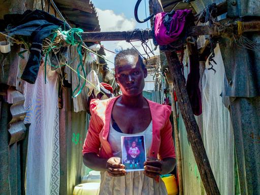 Die Mutter Lumbasi hält ein Foto ihres dreijährigen Sohnes in die Kamera und steht vor einer Hütte in einem Slum in Kenia.