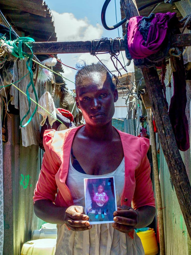 Die Mutter Lumbasi hält ein Foto ihres dreijährigen Sohnes in die Kamera und steht vor einer Hütte in einem Slum in Kenia.
