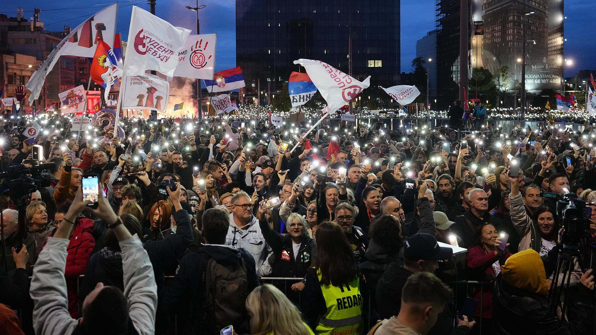 Bei einer Demonstration halten Menschen Fahnen hoch und leuchten mit ihren Handys. 