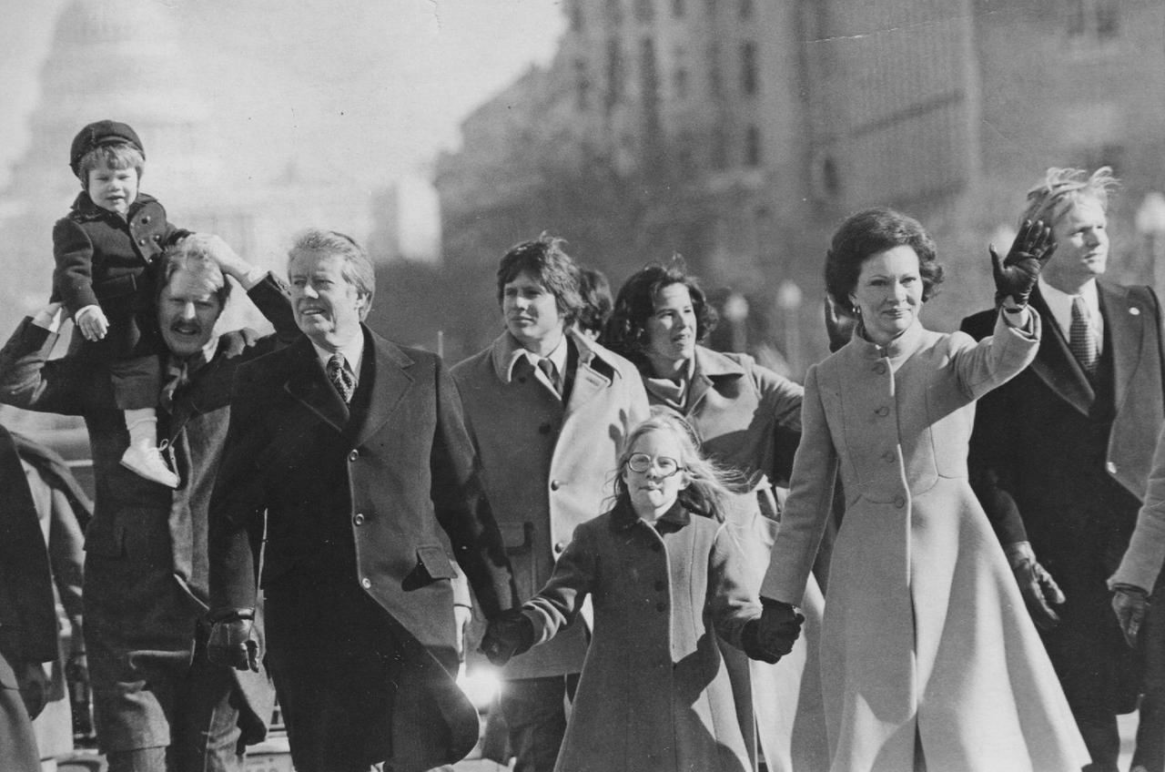 Jimmy Carter, seine Frau Rosalynn und seine Tochter Amy laufen bei der Parade zur Amtseinführung am 20. Januar 1977 umgeben von anderen Personen winkend durch die Straßen von Washington.