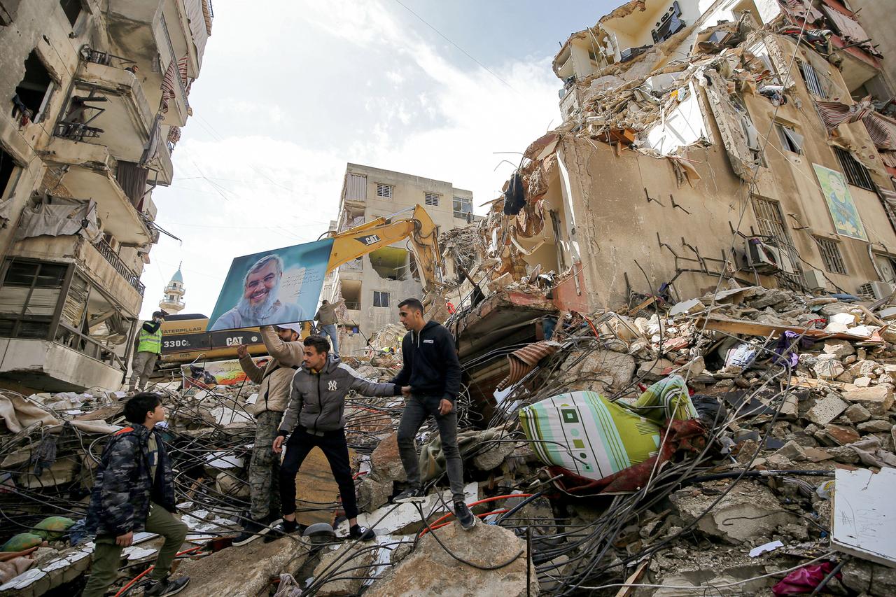 Mehrere Männer stehen auf den Trümmern eines eingestürzten Hauses. Daneben weitere Gebäude.