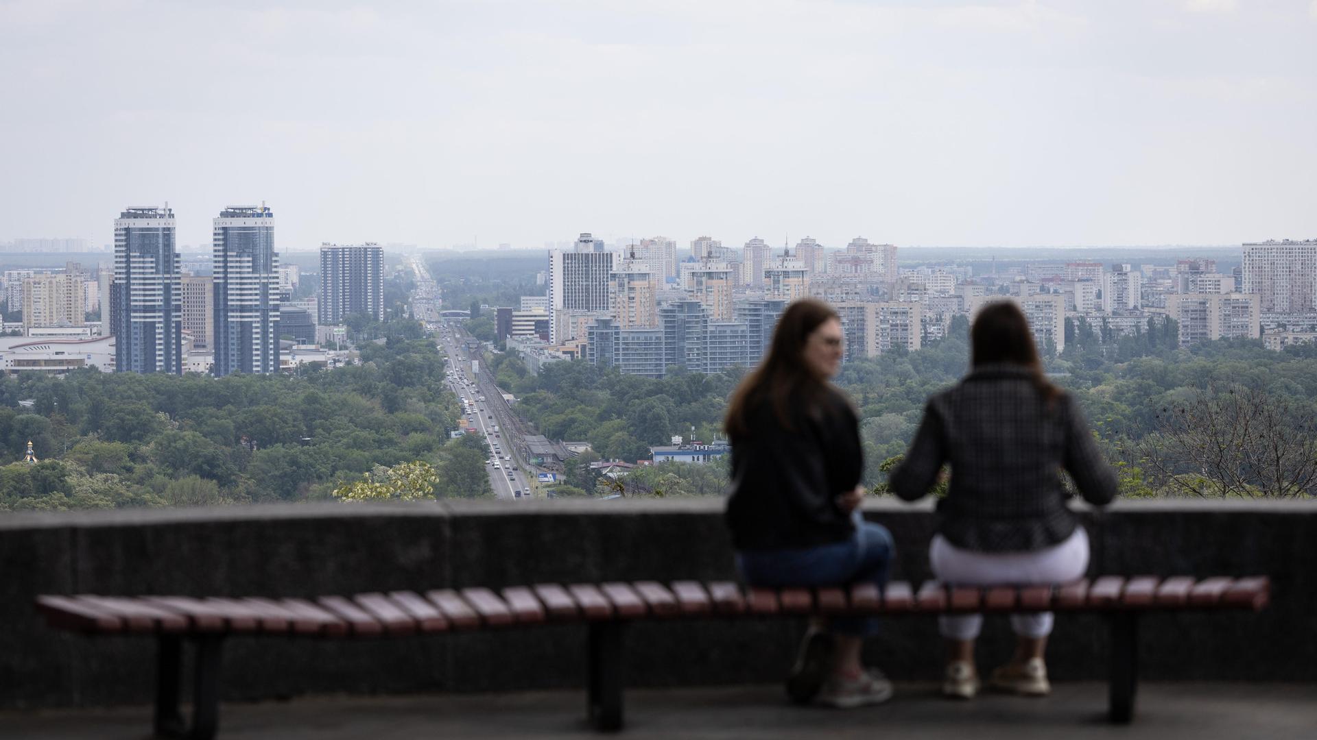 Zwei Frauen sitzen auf einer Bank im Vechnoi-Slavy-Park im Zentrum von Kiew und unterhalten sich.