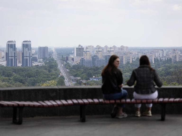 Zwei Frauen sitzen auf einer Bank im Vechnoi-Slavy-Park im Zentrum von Kiew und unterhalten sich.