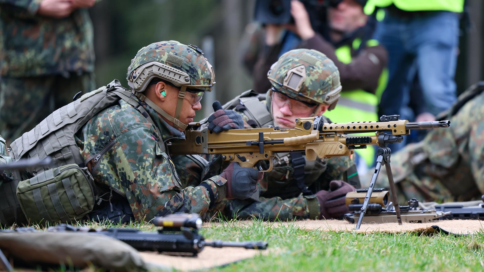 Zwei Bundeswehr-Soldaten liegen auf dem Boden. Sie tragen Uniform und Helme. Vor ihnen steht ein Gewehr. 