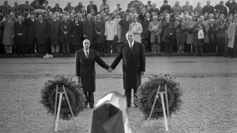 Bundeskanzler Helmut Kohl (r.) und der französische Staatspräsident François Mitterrand stehen bei einer Feierstunde in Verdun und reichen sich die Hände.