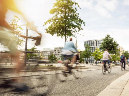 Straßenszene in einer Stadt mit auf einem breiten Fahrradweg fahrenden Fahrradfahrern.