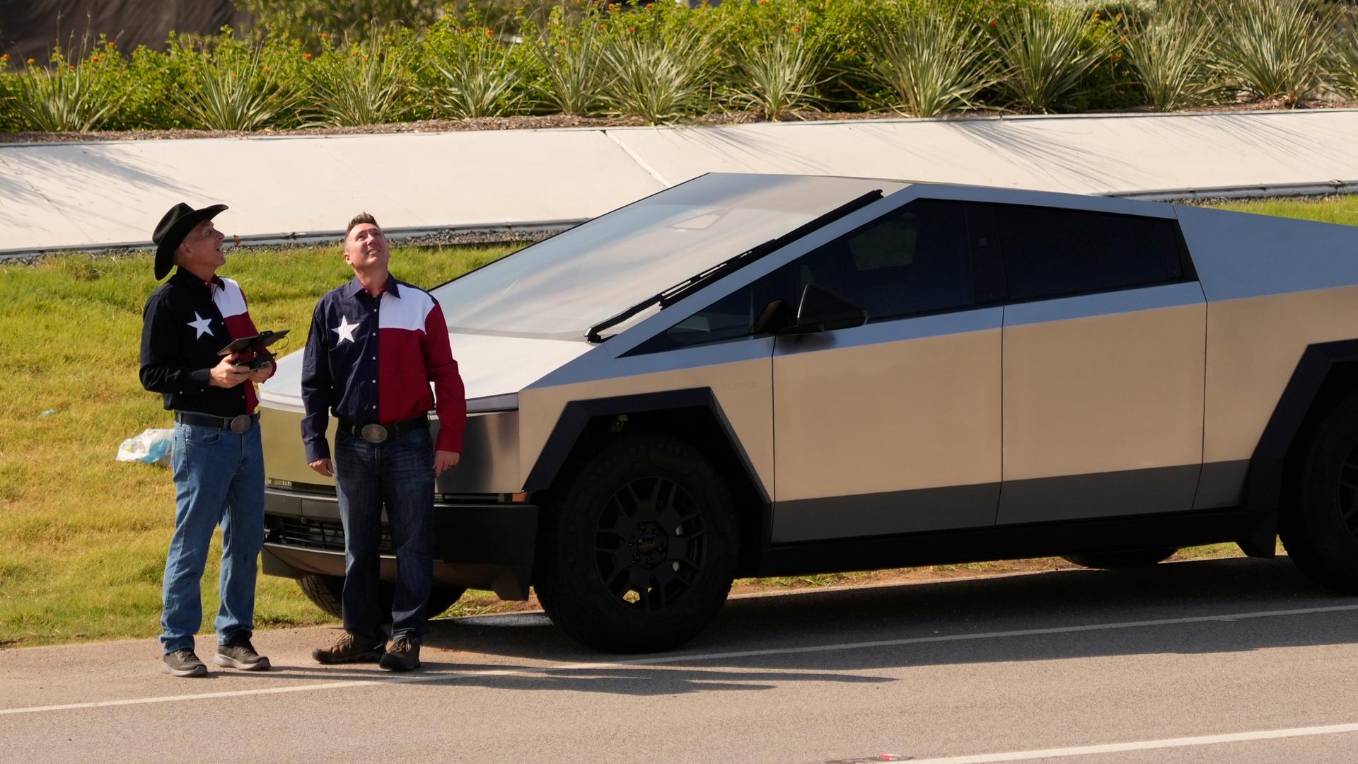 Zwei Männer in Westernhemden mit texanischer Flagge stehen neben einem Tesla Cybertruck vor derTesla Gigafactory in Austin, Texas.