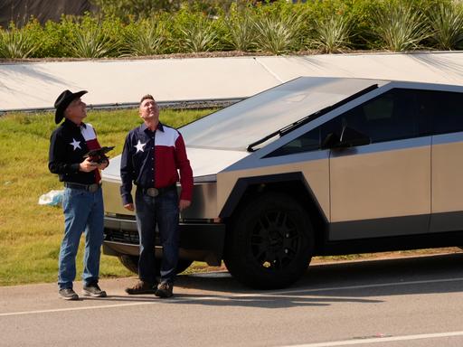 Zwei Männer in Westernhemden mit texanischer Flagge stehen neben einem Tesla Cybertruck vor derTesla Gigafactory in Austin, Texas.