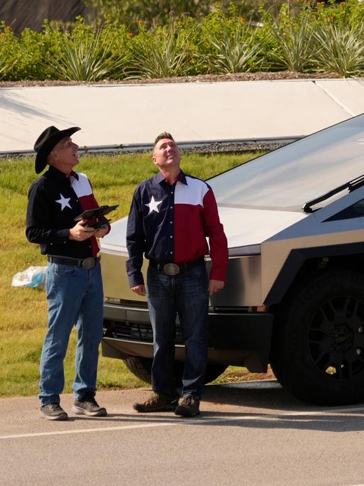 Zwei Männer in Westernhemden mit texanischer Flagge stehen neben einem Tesla Cybertruck vor derTesla Gigafactory in Austin, Texas.