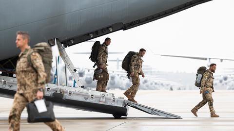 Soldaten in beiger Tarnkleidung steigen über die Laderampe aus einem Flugzeug der Bundeswehr.