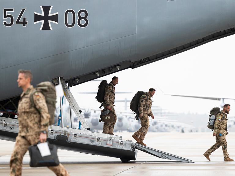 Soldaten in beiger Tarnkleidung steigen über die Laderampe aus einem Flugzeug der Bundeswehr.