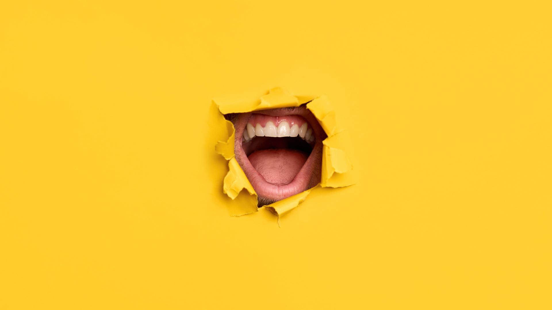 Ein offener, schreiender Mund bricht durch eine gelbe Papierwand